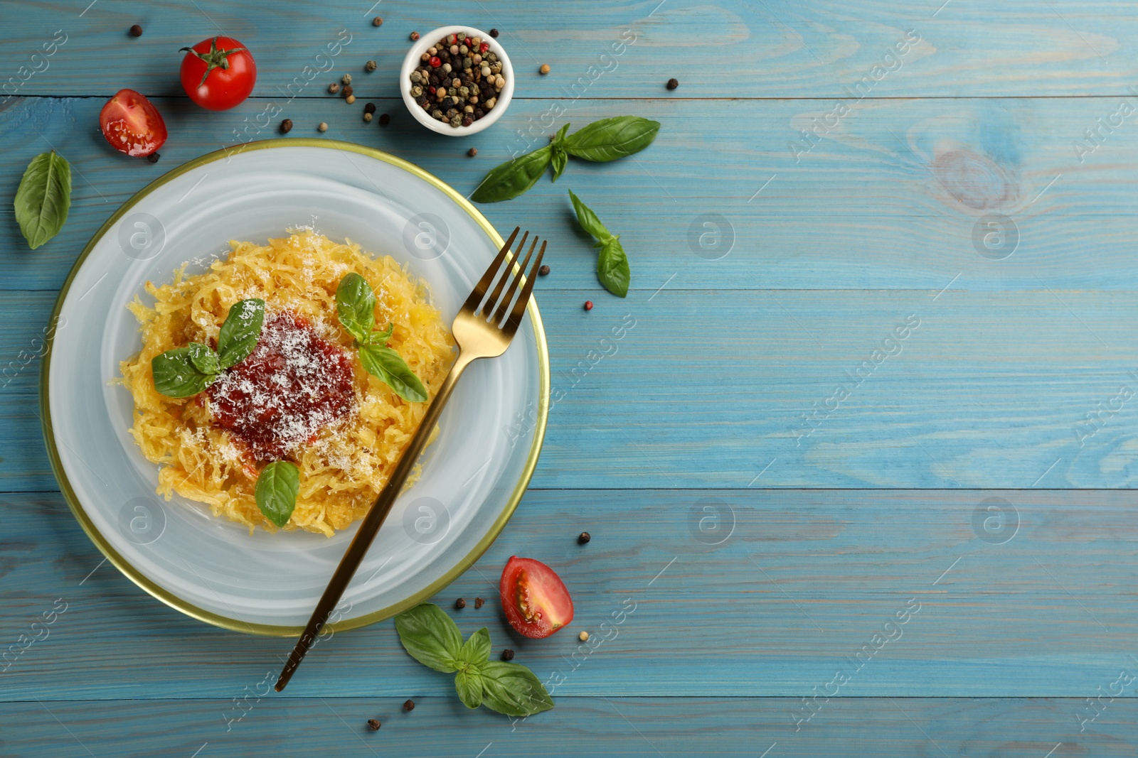 Photo of Tasty spaghetti squash with tomato sauce, cheese and basil served on light blue wooden table, flat lay. Space for text