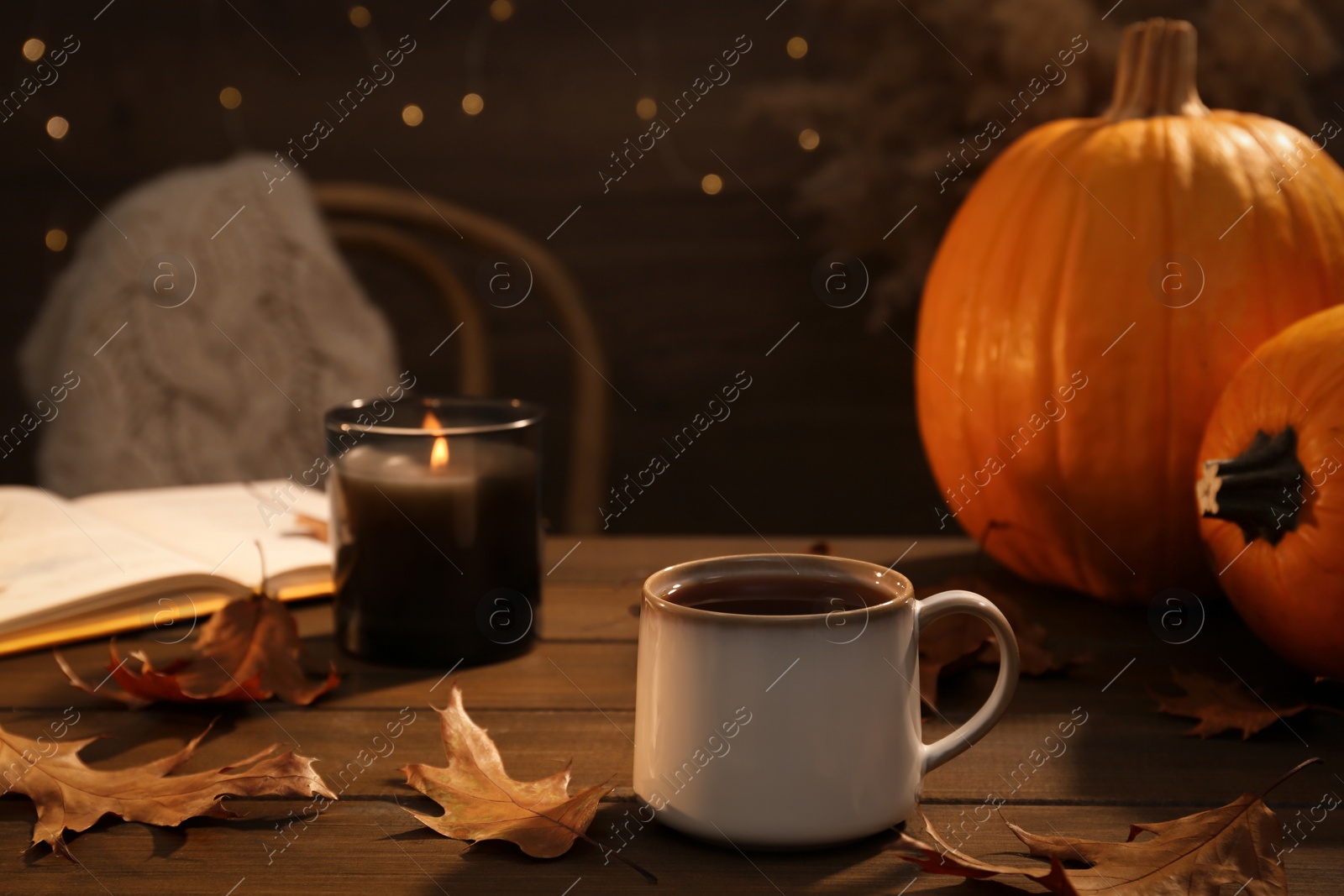 Photo of Cup of aromatic tea, candle, pumpkins and autumn leaves on wooden table indoors. Space for text
