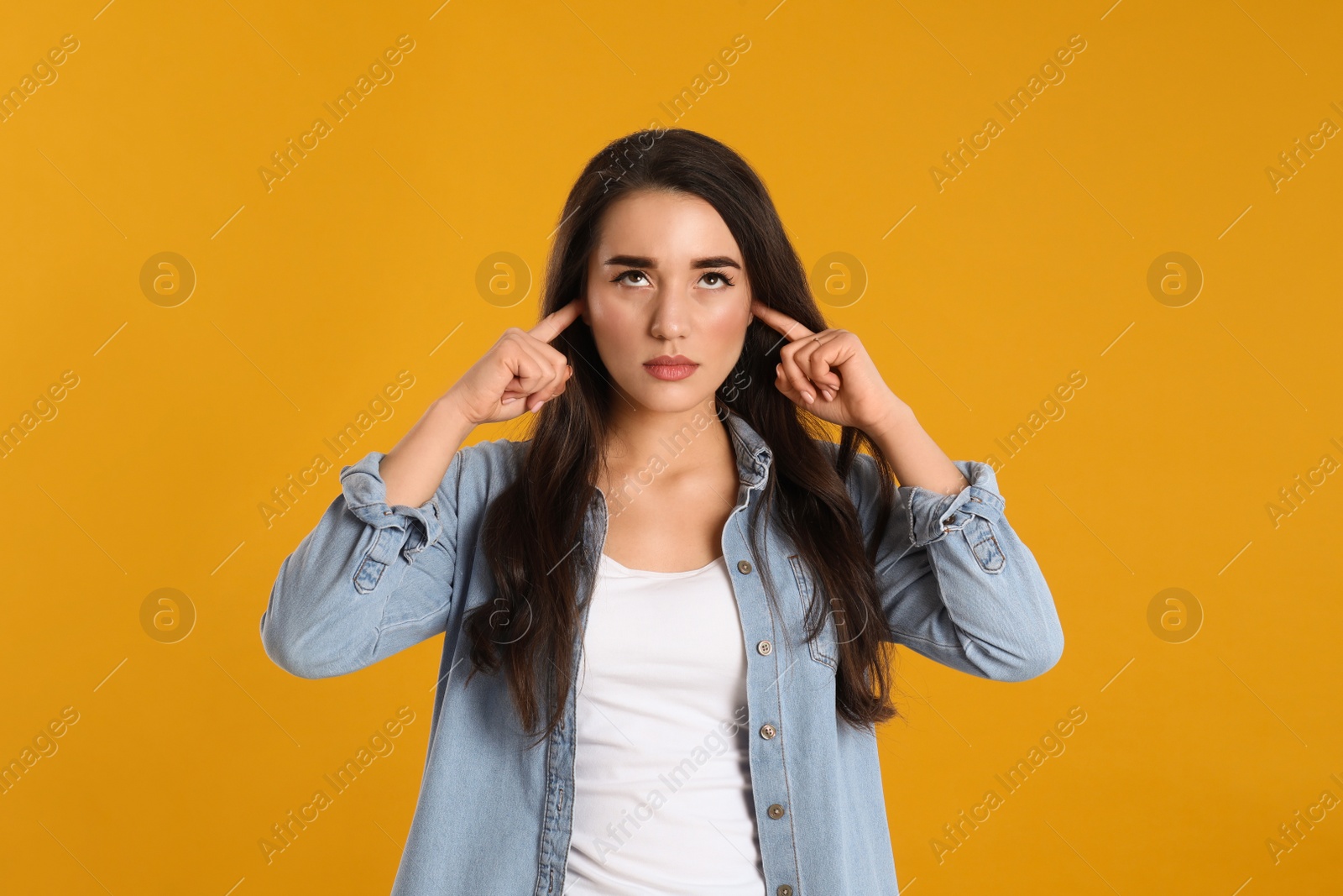 Photo of Young woman covering ears with fingers on yellow background