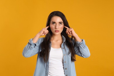 Young woman covering ears with fingers on yellow background