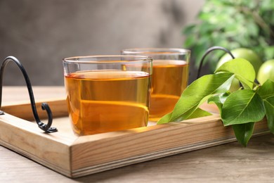 Glasses of fresh apple juice and leaves on wooden table