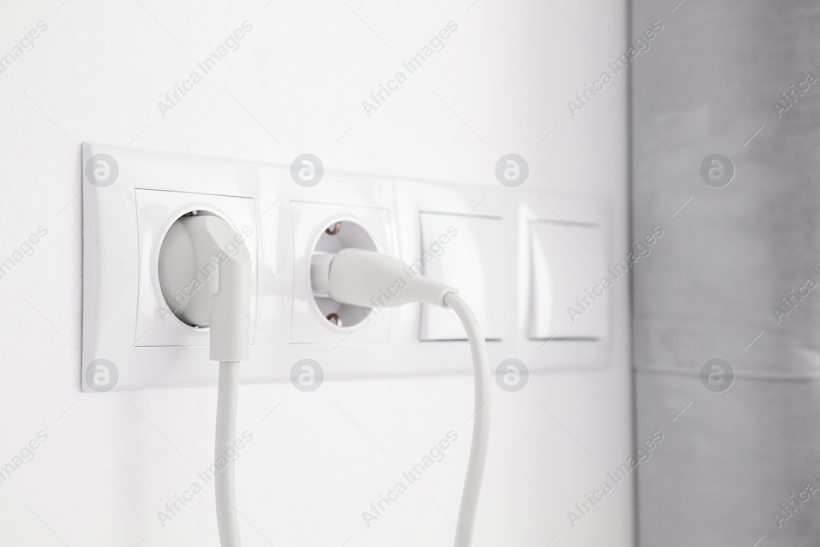 Photo of Power sockets with inserted plugs and light switches on white wall indoors