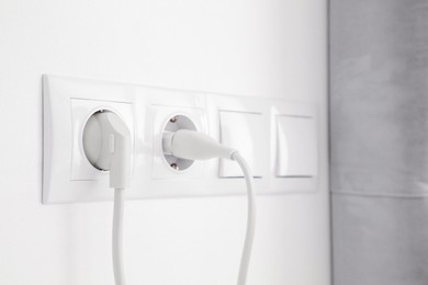 Photo of Power sockets with inserted plugs and light switches on white wall indoors