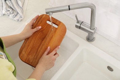 Photo of Woman washing wooden cutting board at sink in kitchen, closeup