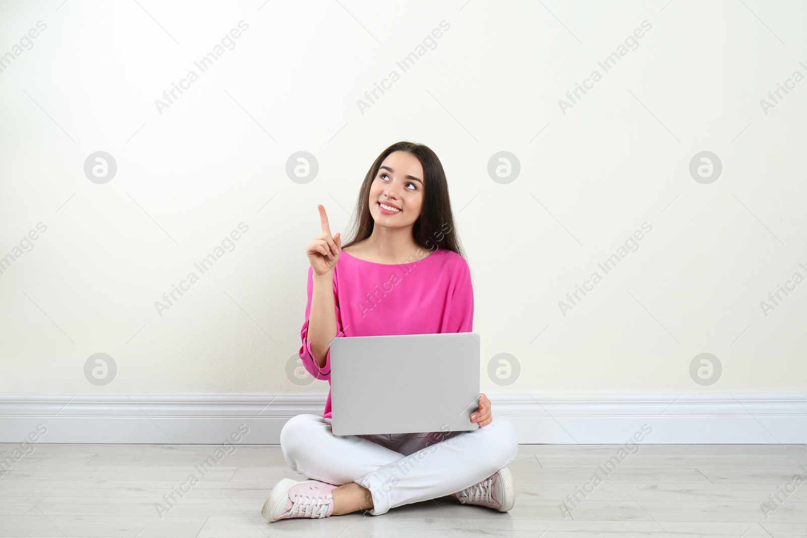 Photo of Young woman with laptop sitting on floor near light wall indoors