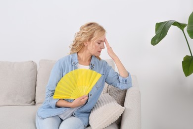 Photo of Woman waving hand fan to cool herself at home. Hormonal disorders