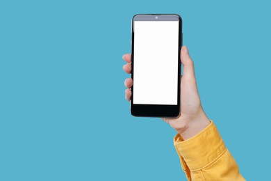 Photo of Woman holding smartphone with blank screen on light blue background, closeup. Mockup for design