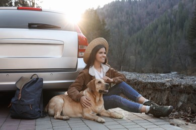 Happy woman and adorable dog sitting near car in mountains. Traveling with pet