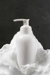 Photo of Dispenser with cleansing foam on dark grey background, closeup. Cosmetic product