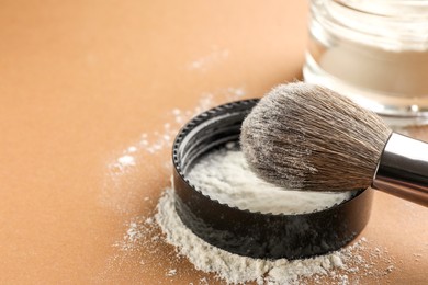 Photo of Makeup brush and lid with rice loose face powder on brown background, closeup. Space for text