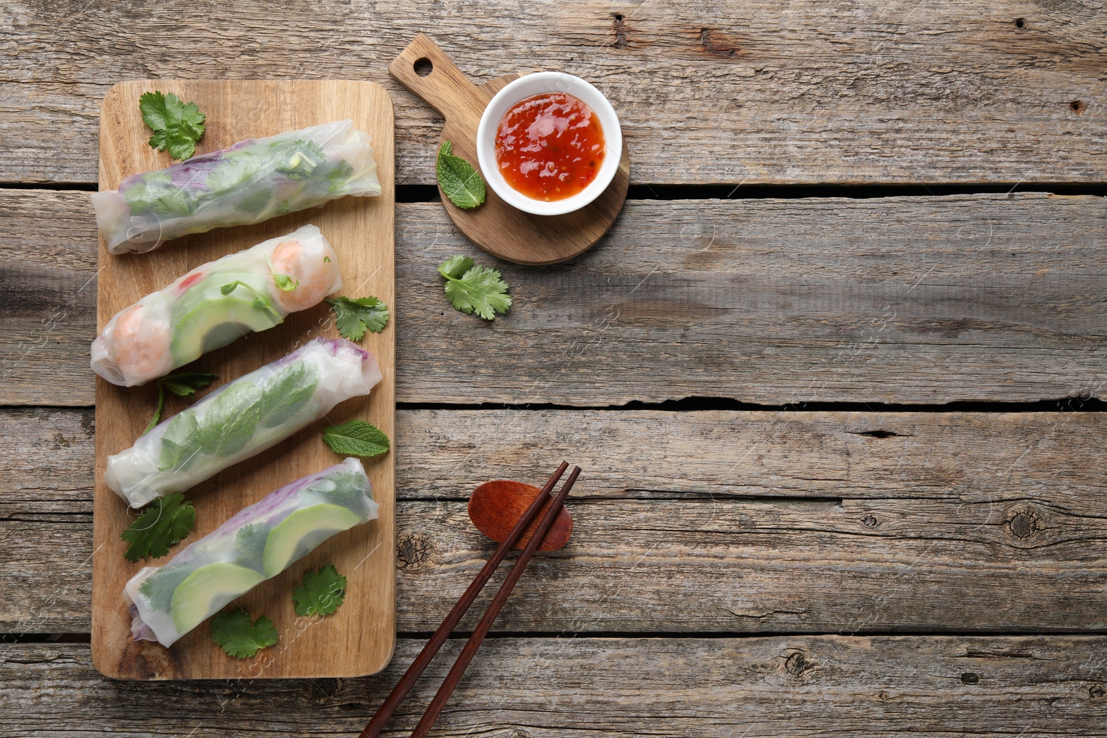 Photo of Delicious spring rolls, sauce and chopsticks on wooden table, top view. Space for text