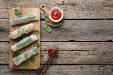 Delicious spring rolls, sauce and chopsticks on wooden table, top view. Space for text