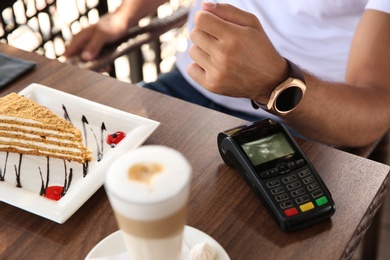 Photo of Man making payment with smart watch in cafe, closeup