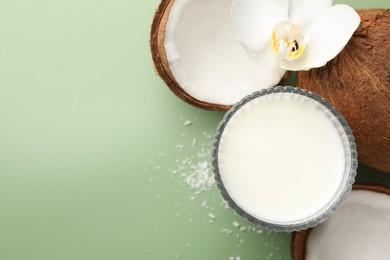 Photo of Glass of delicious vegan milk, coconuts and flower on green background, flat lay. Space for text