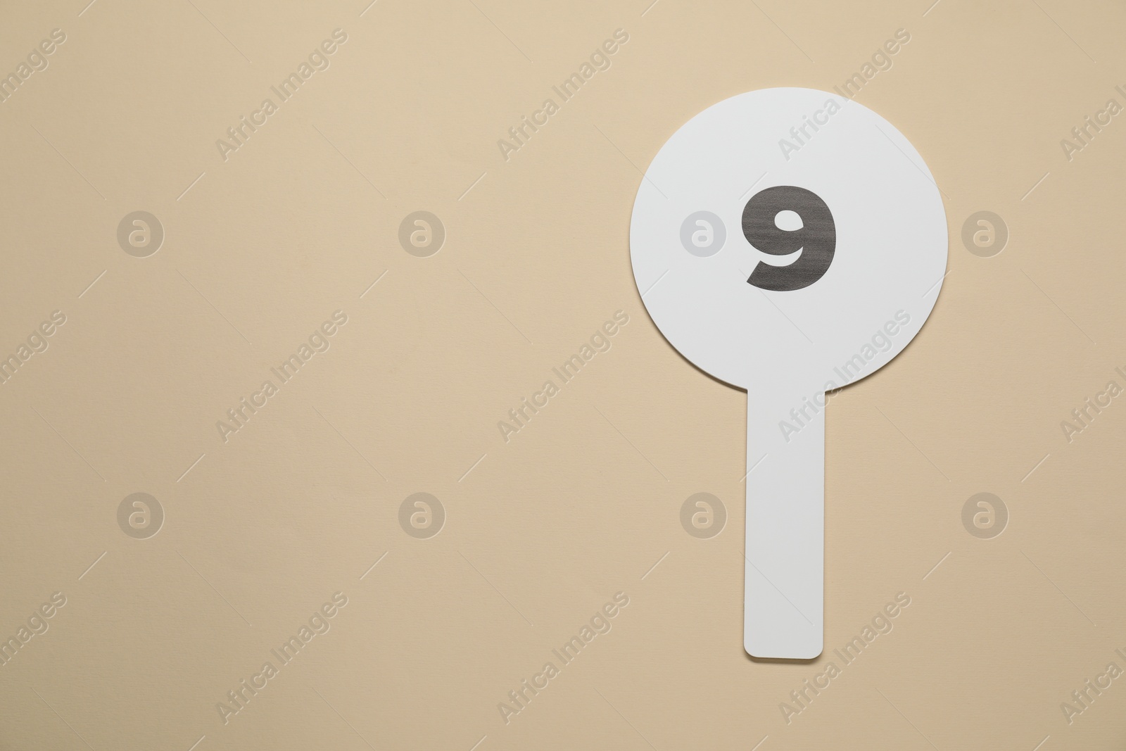 Photo of Auction paddle with number 9 on beige background, top view. Space for text