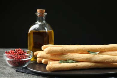 Photo of Fresh delicious grissini sticks with rosemary, oil and red peppercorns on black table