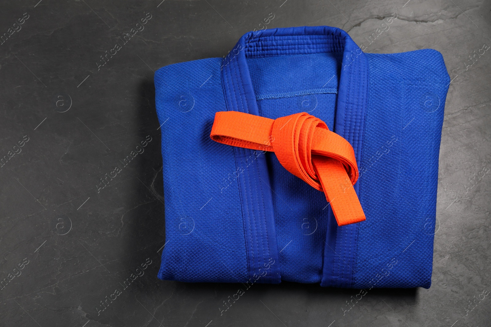 Photo of Orange karate belt and blue kimono on gray background, top view. Space for text