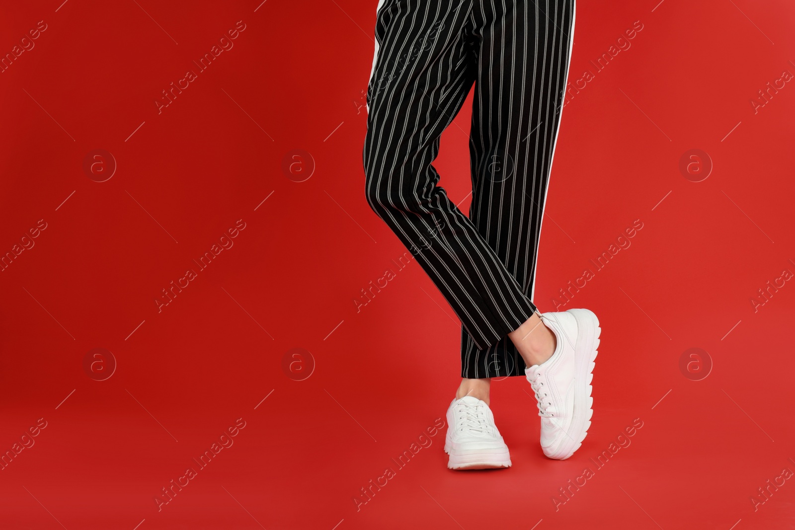 Photo of Woman in stylish sport shoes on red background. Space for text