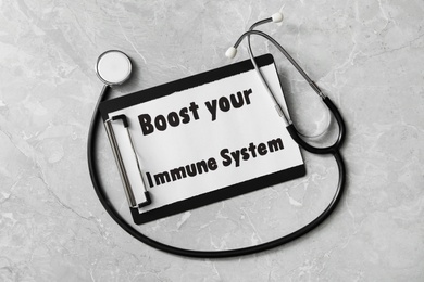 Clipboard with words Boost Your Immune System and stethoscope on light grey table, flat lay