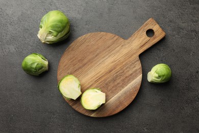Photo of Wooden cutting board and Brussels sprouts on dark textured table, top view