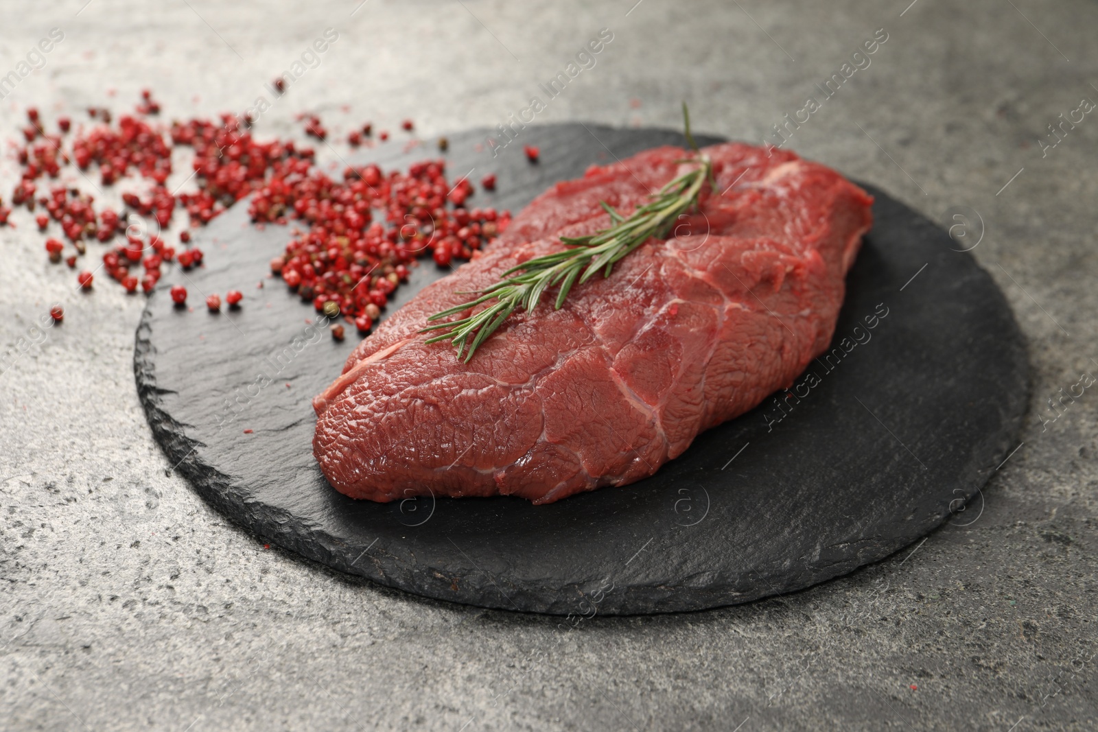 Photo of Piece of raw beef meat, rosemary and red peppercorns on grey table, closeup