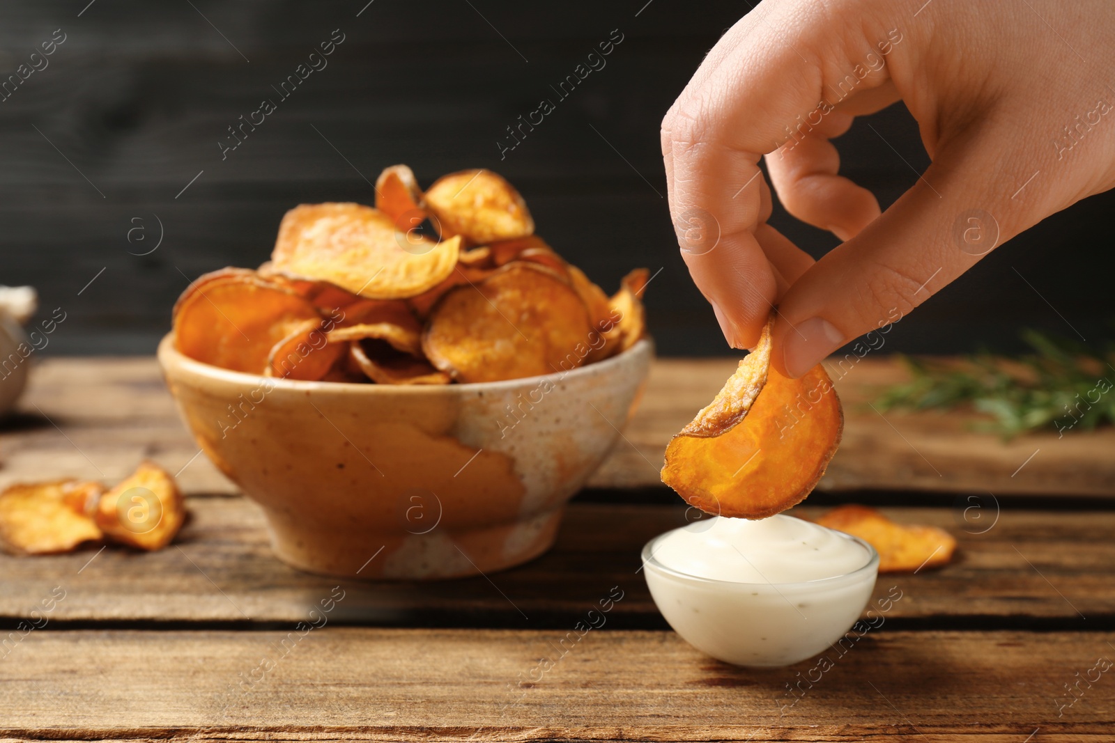 Photo of Woman dipping sweet potato chip into sauce on table, closeup