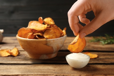 Woman dipping sweet potato chip into sauce on table, closeup