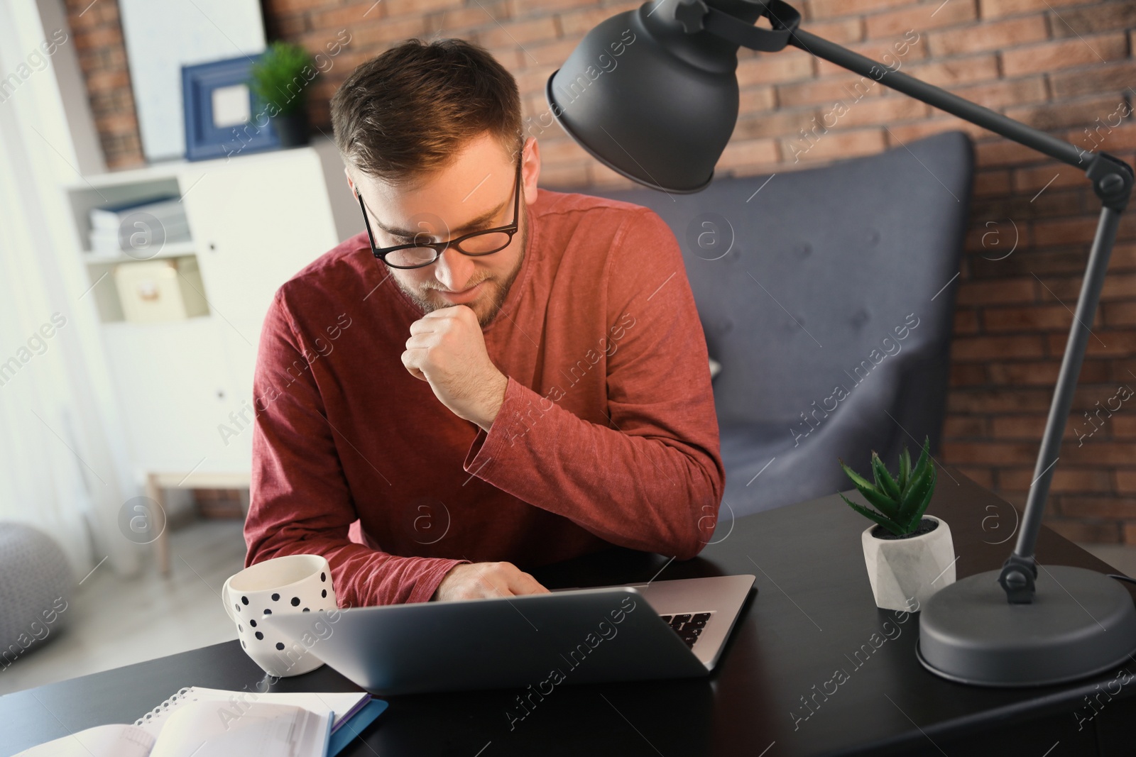 Photo of Young man using laptop at table indoors