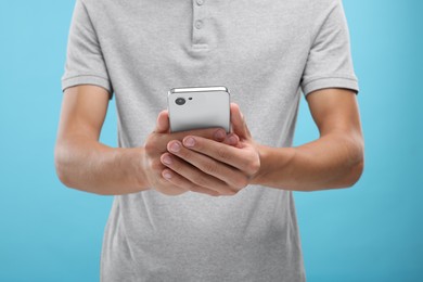 Photo of Young man sending message via smartphone on light blue background, closeup