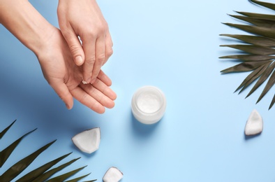 Photo of Young woman applying coconut oil on color background, closeup