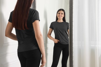 Photo of Beautiful young woman in stylish black jeans near mirror indoors