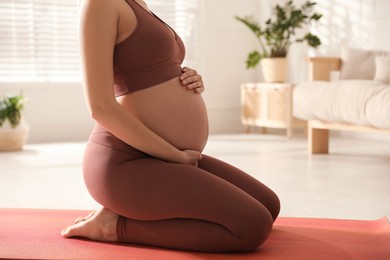 Photo of Young pregnant woman practicing yoga at home, closeup