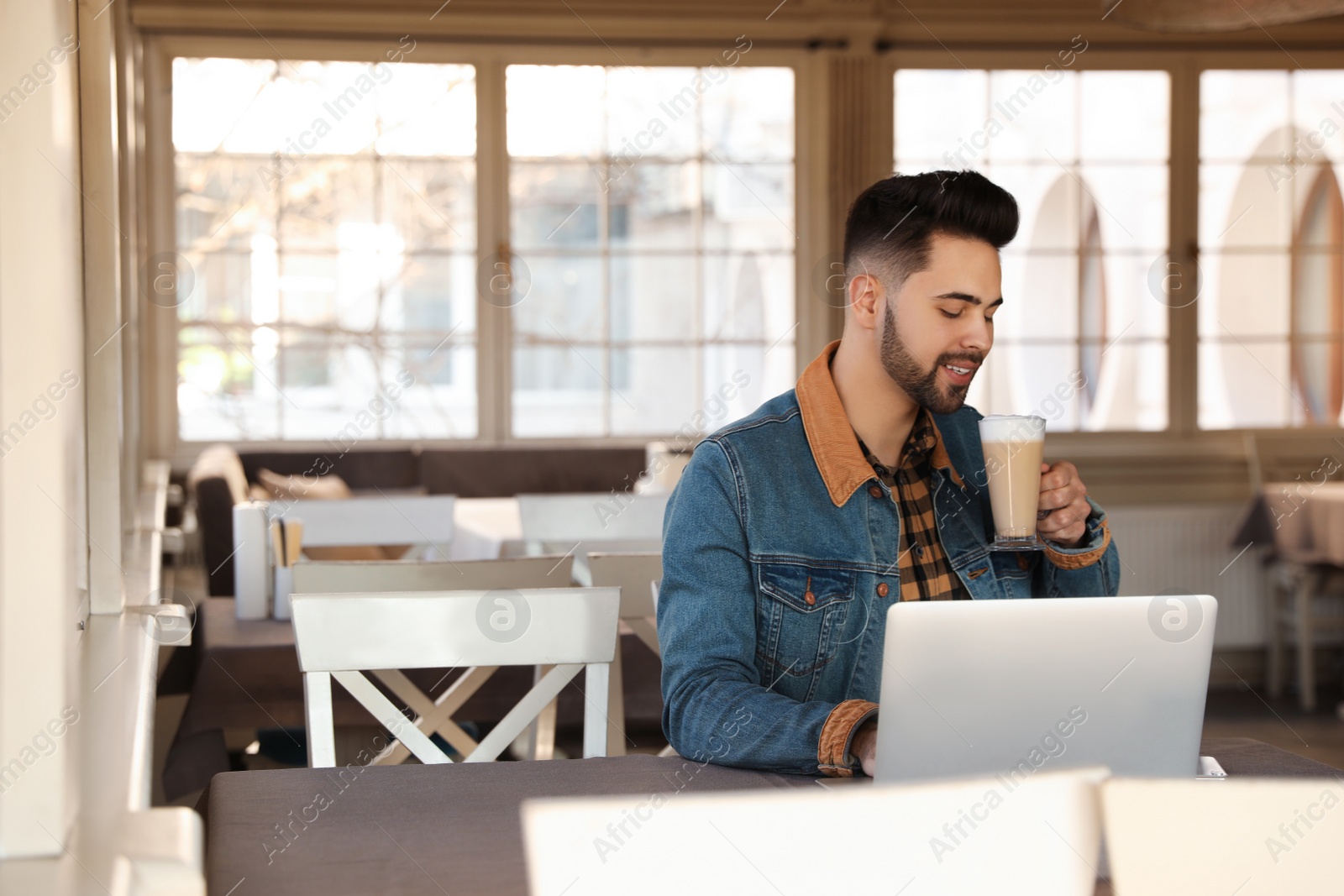 Photo of Young blogger with laptop drinking latte at table in cafe. Space for text