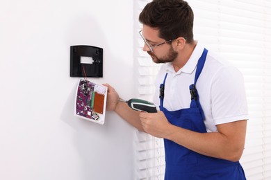 Technician installing home security alarm system on white wall indoors