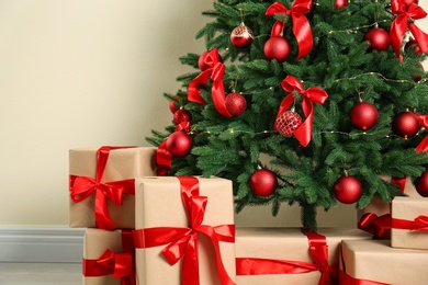 Decorated Christmas tree and gift boxes near beige wall