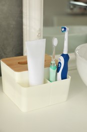 Electric toothbrushes and tube of paste near vessel sink on countertop in bathroom