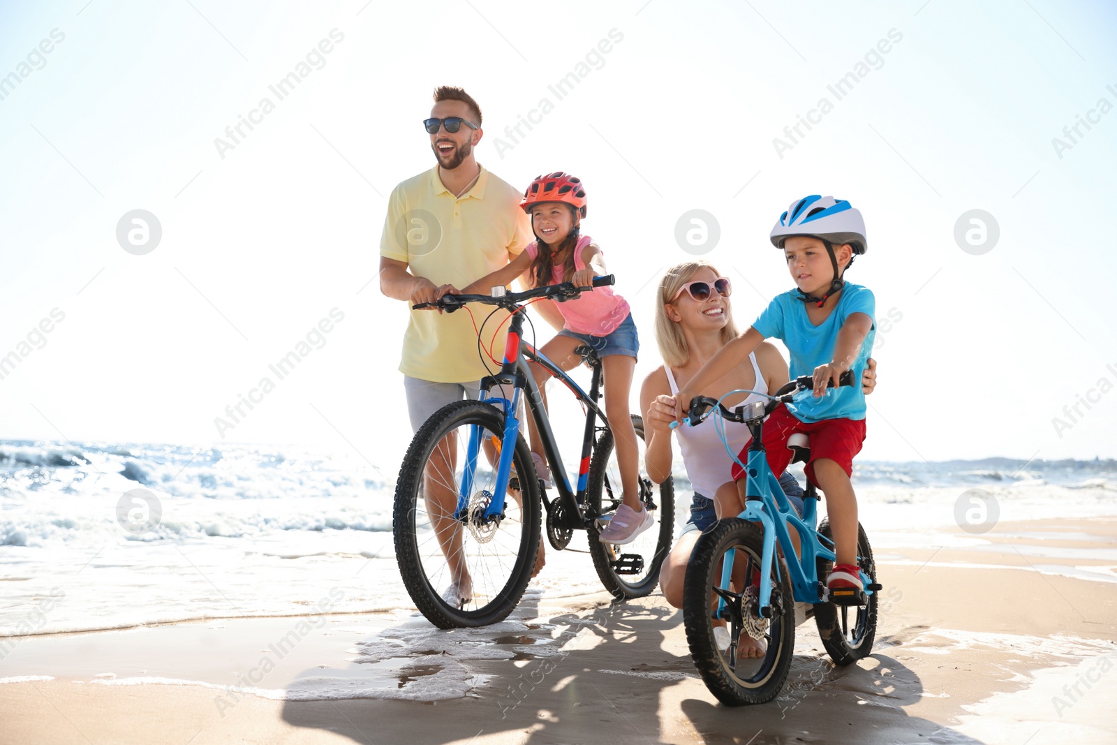 Photo of Happy parents teaching children to ride bicycles on sandy beach near sea