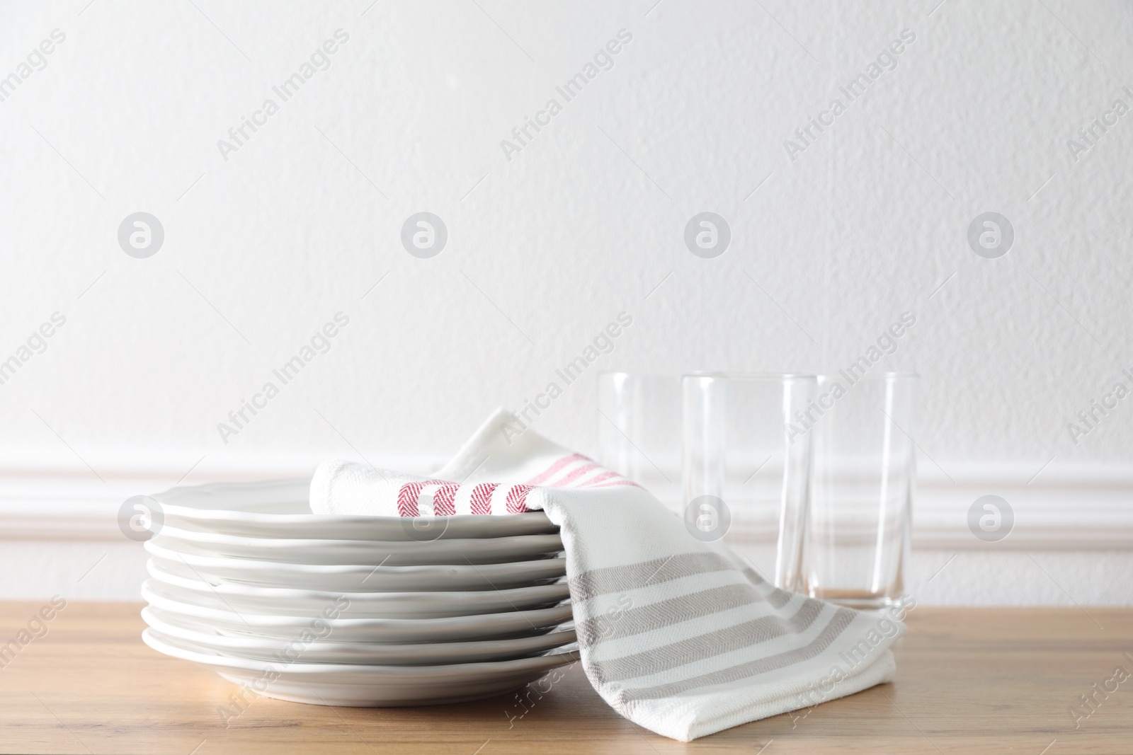 Photo of Kitchen towel and clean dishware on wooden table near white wall