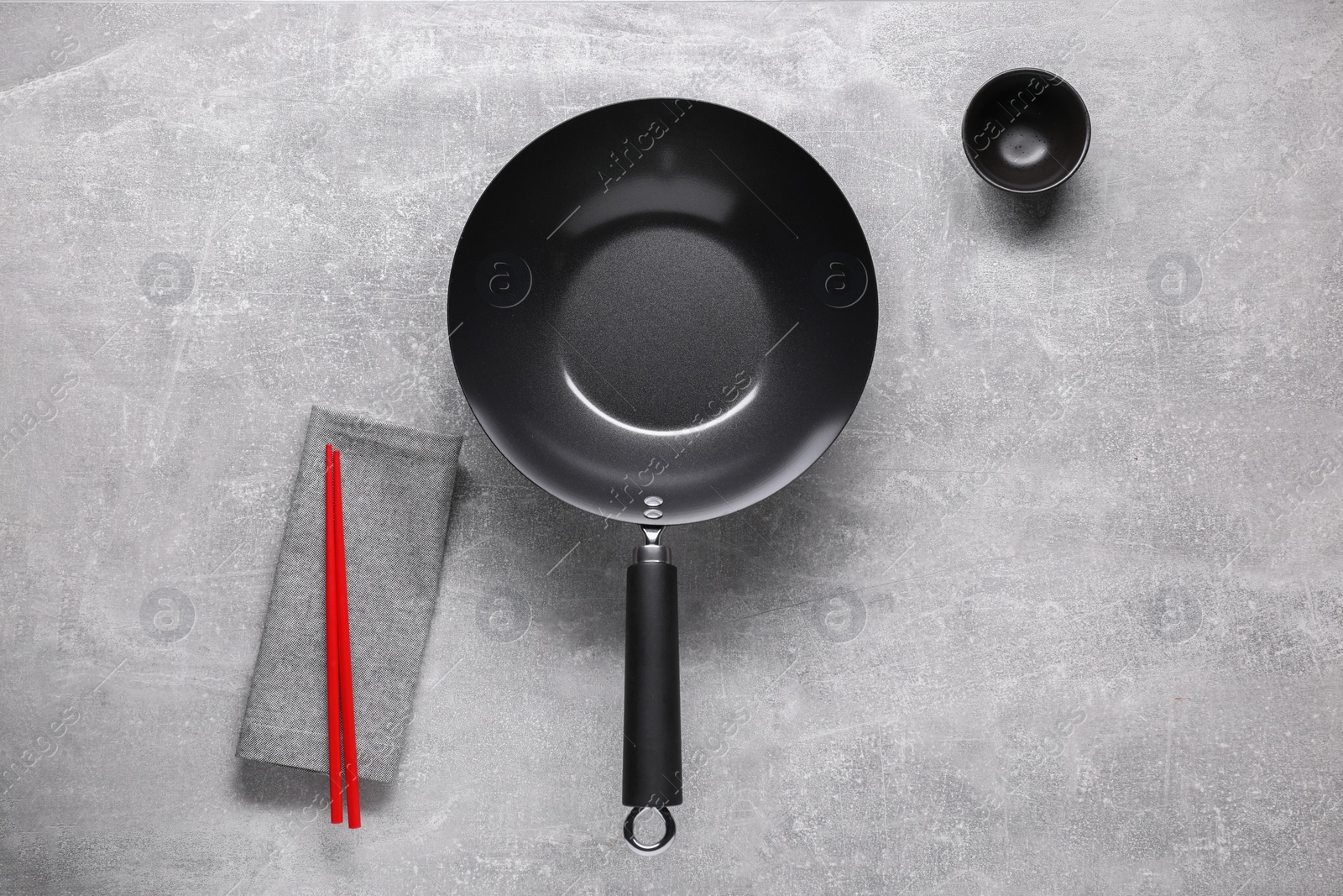 Photo of Empty iron wok, sauce bowl and chopsticks on grey table, flat lay