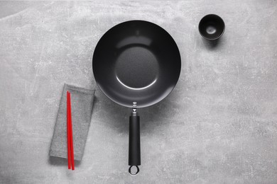 Empty iron wok, sauce bowl and chopsticks on grey table, flat lay