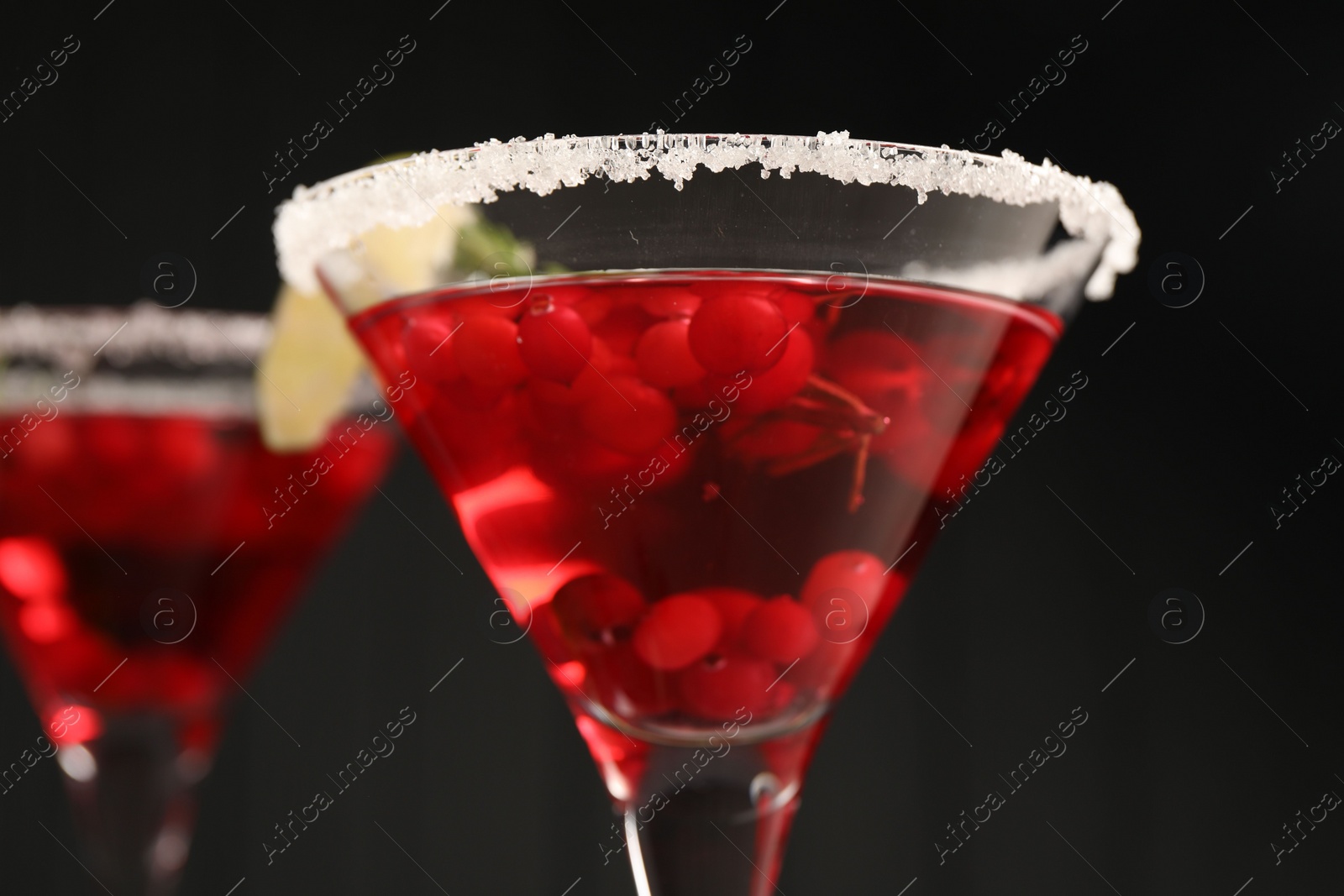 Photo of Tasty cranberry cocktail in glasses against black background, closeup