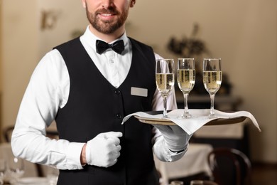 Photo of Butler holding tray with glasses of sparkling wine in restaurant, closeup