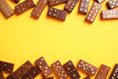 Wooden domino tiles on yellow background, flat lay. Space for text