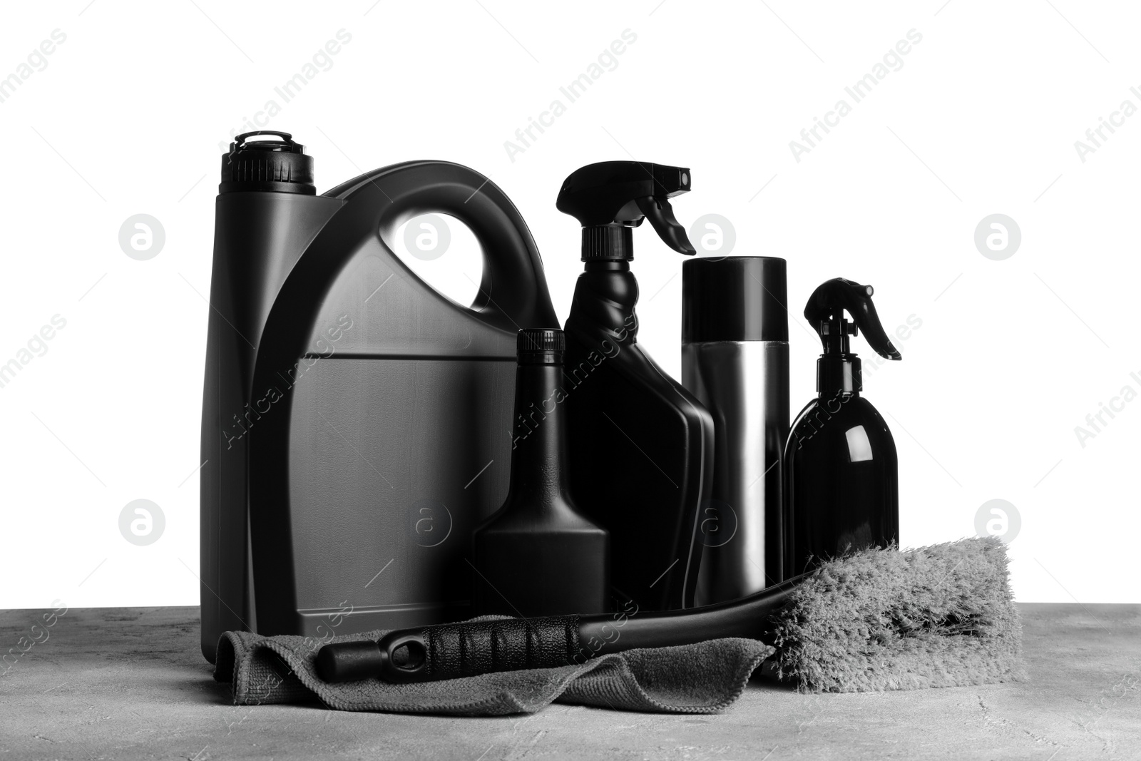 Photo of Bottles, brush and car wash cloth on grey table against white background