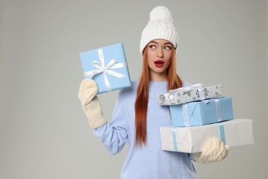 Photo of Emotional young woman in hat and sweater with Christmas gifts on light grey background