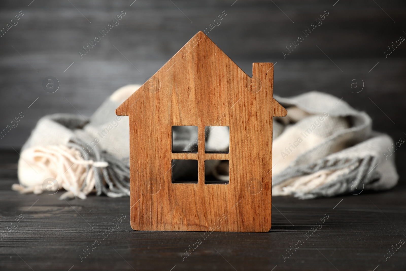 Photo of Wooden house model and scarf on grey table. Heating efficiency