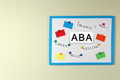 Board with abbreviation ABA and different colors on beige wall, space for text