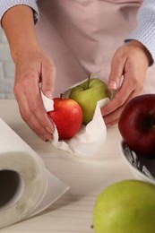 Photo of Woman wiping apples with paper towel at light wooden table, closeup