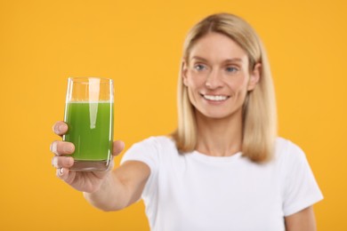 Photo of Happy woman with glass of fresh celery juice on orange background, selective focus