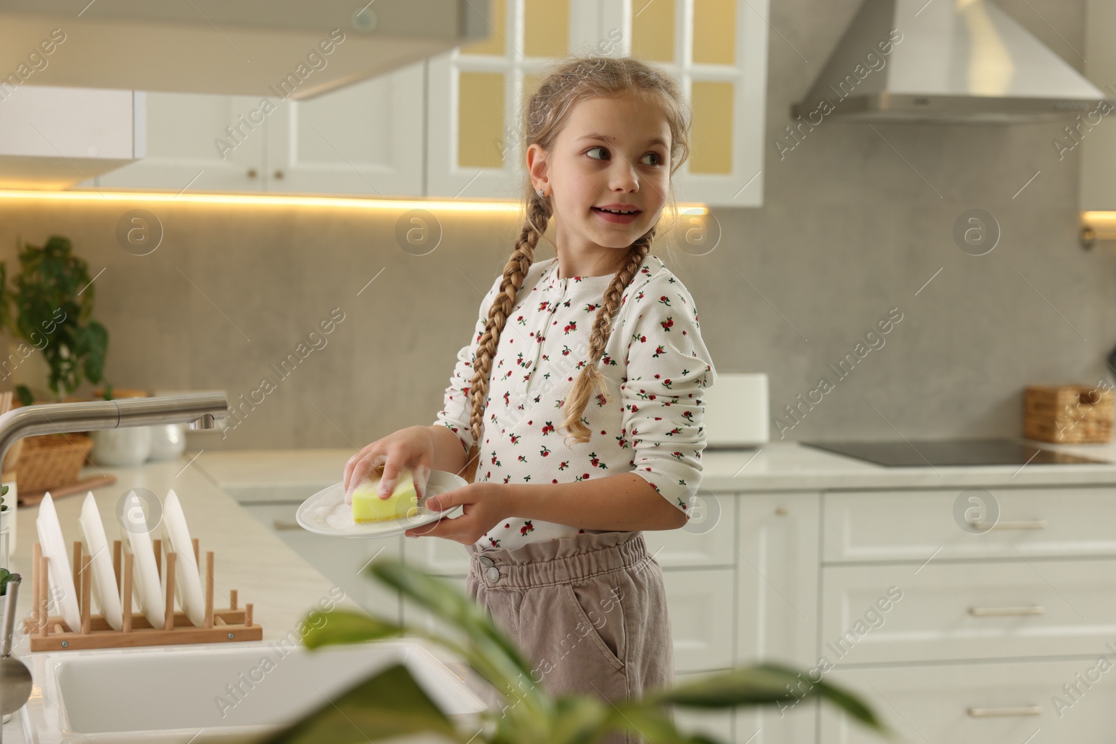 Photo of Little girl washing plate above sink in kitchen